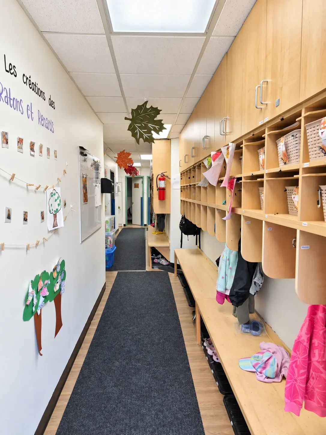 Long vestiaire avec casiers en bois, bancs et bottes, et des bricolages d’enfants affichés sur le mur opposé